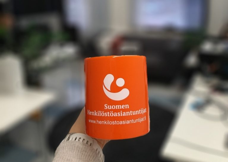 Kädessä pidetään oranssia mukia Suomen Henkilöstöasiantuntijoiden toimistossa.