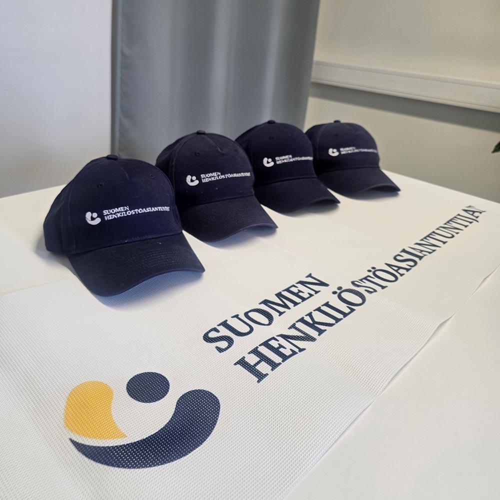 Suomen Henkilöstöasiantuntijoiden logo ja neljä mustaa lippalakkia pöydällä.